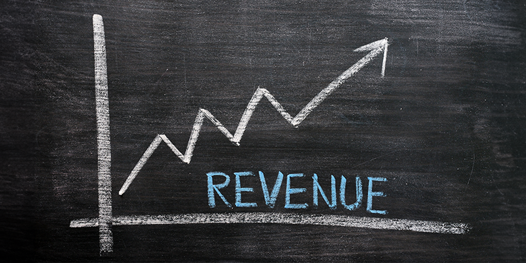 An upward graph drawn on a blackboard with white chalk. The word revenue is written underneath it with blue chalk.