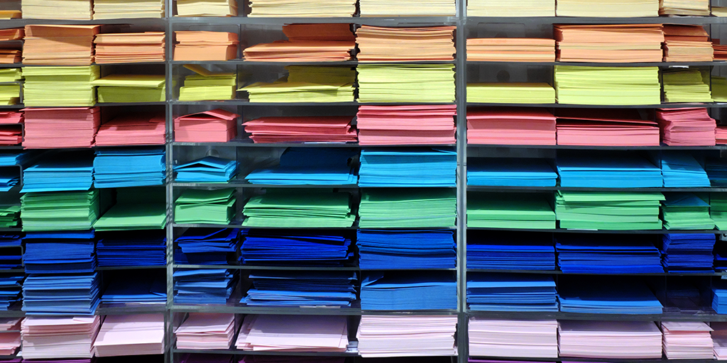 A shelf with stacks of papers in different colors.