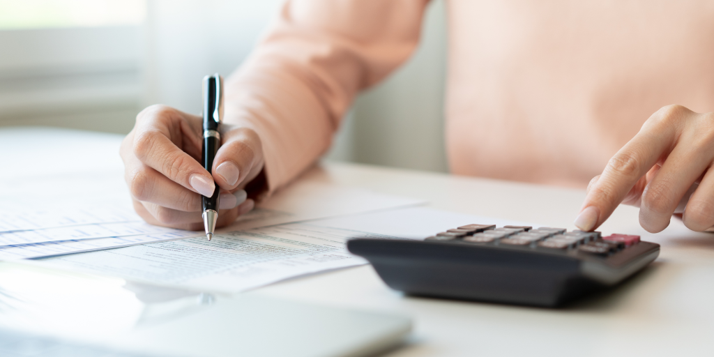 A person using a calculator and using a pen to write down the results on a sheet of paper.